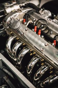 A person examining a diesel engine with the hood open and visible engine components outdoors.