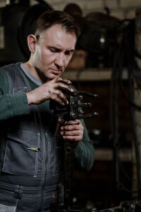 A mechanic in coveralls inspecting the engine bay of a modern pickup truck inside a well-lit garage.